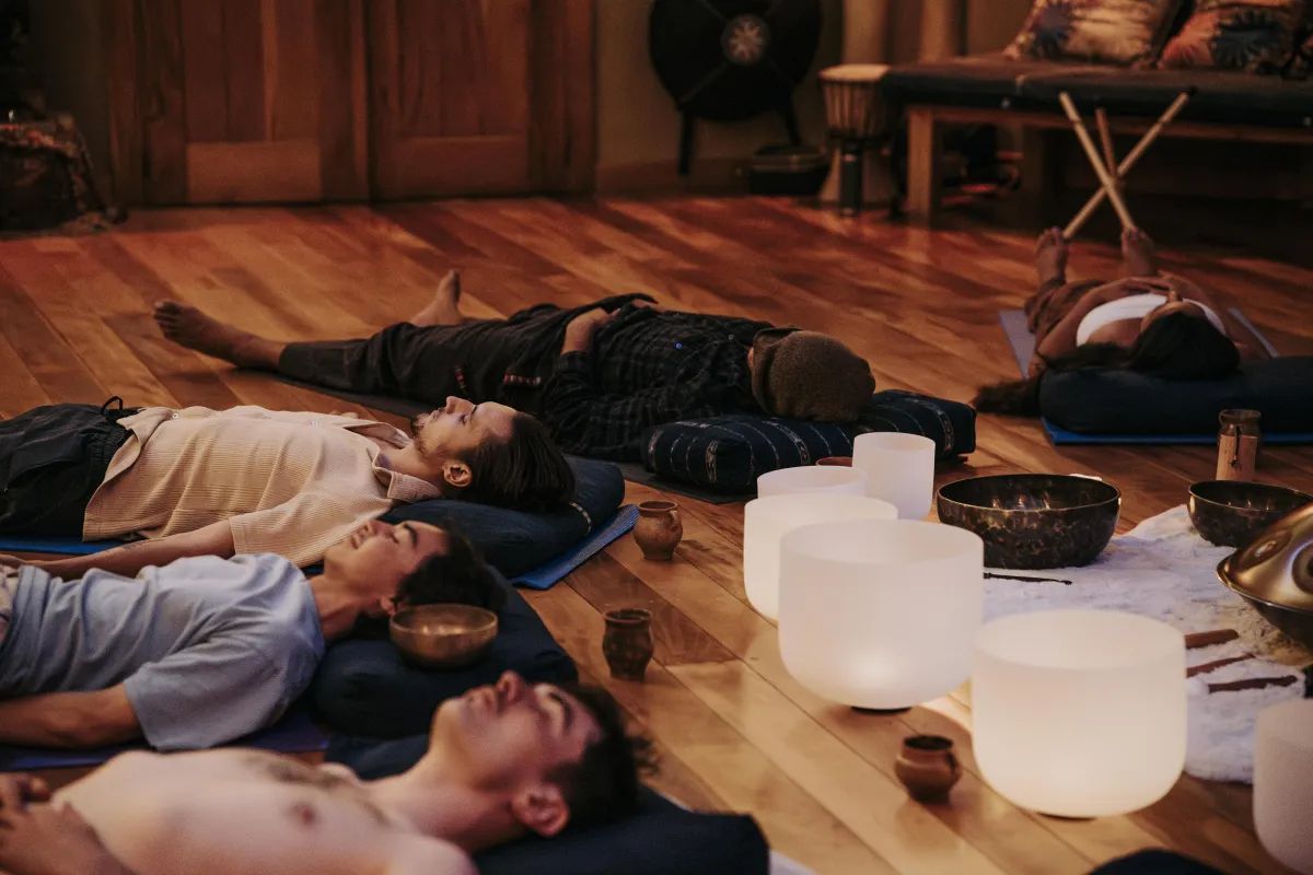 People lying on mats in a warm, candlelit room with crystal singing bowls glowing beside them