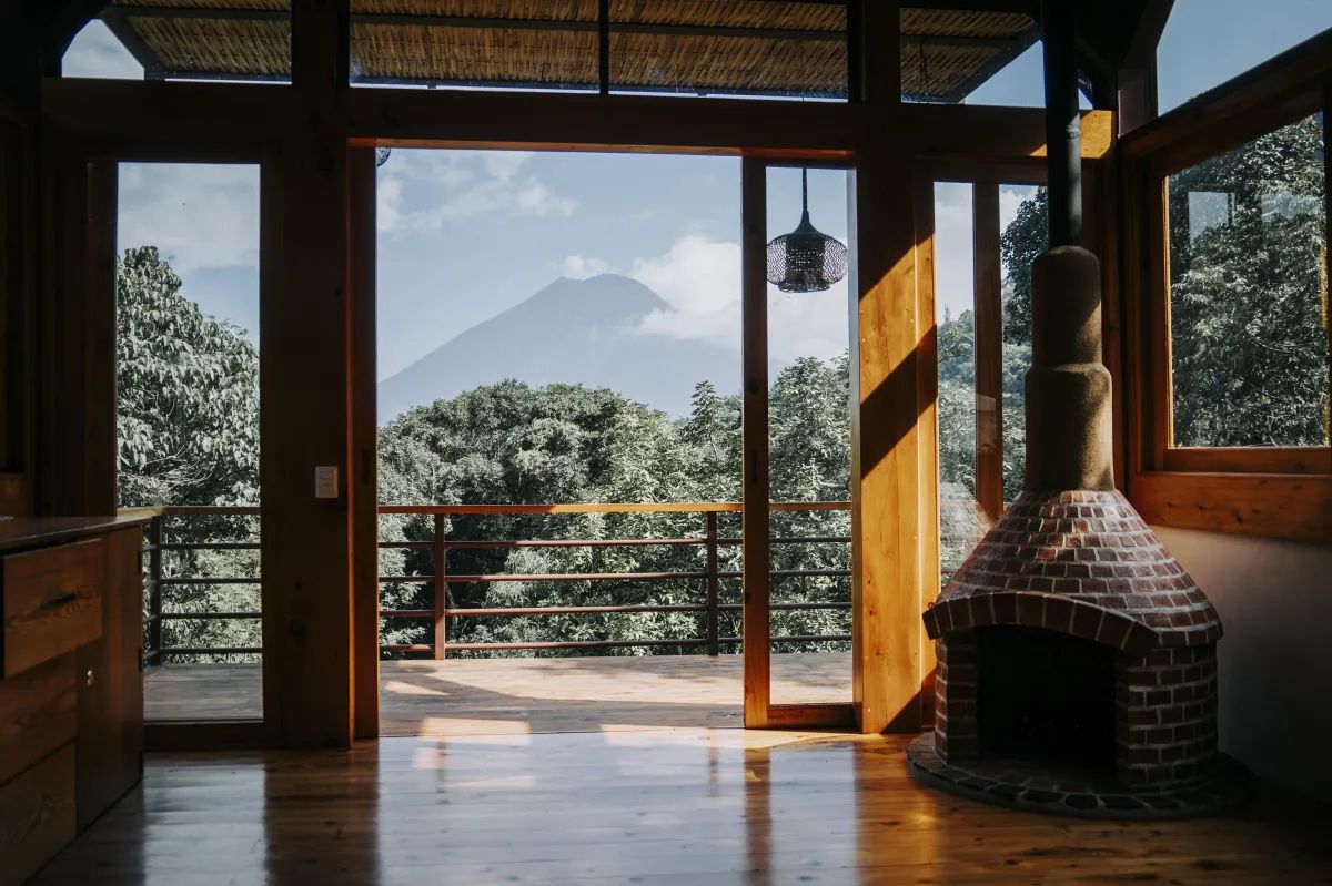 The view of a volcano through open timber doors beside a brick fireplace